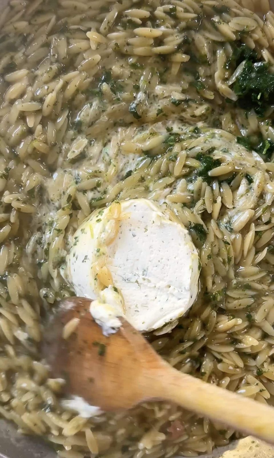 Stiirring Boursin into lemon chicken orzo with wood spoon.