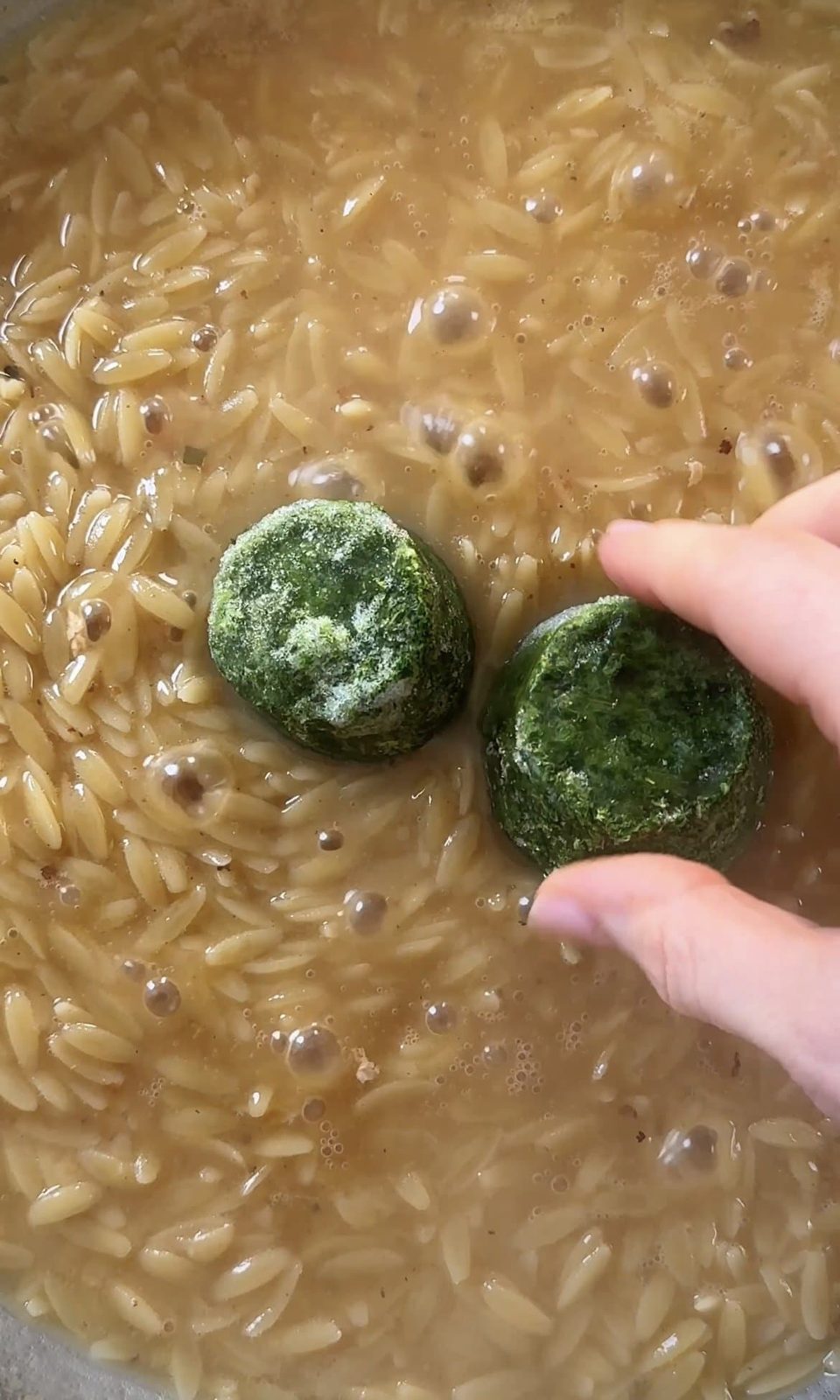 Adding frozen spinach cubes to pan with orzo and chicken stock.