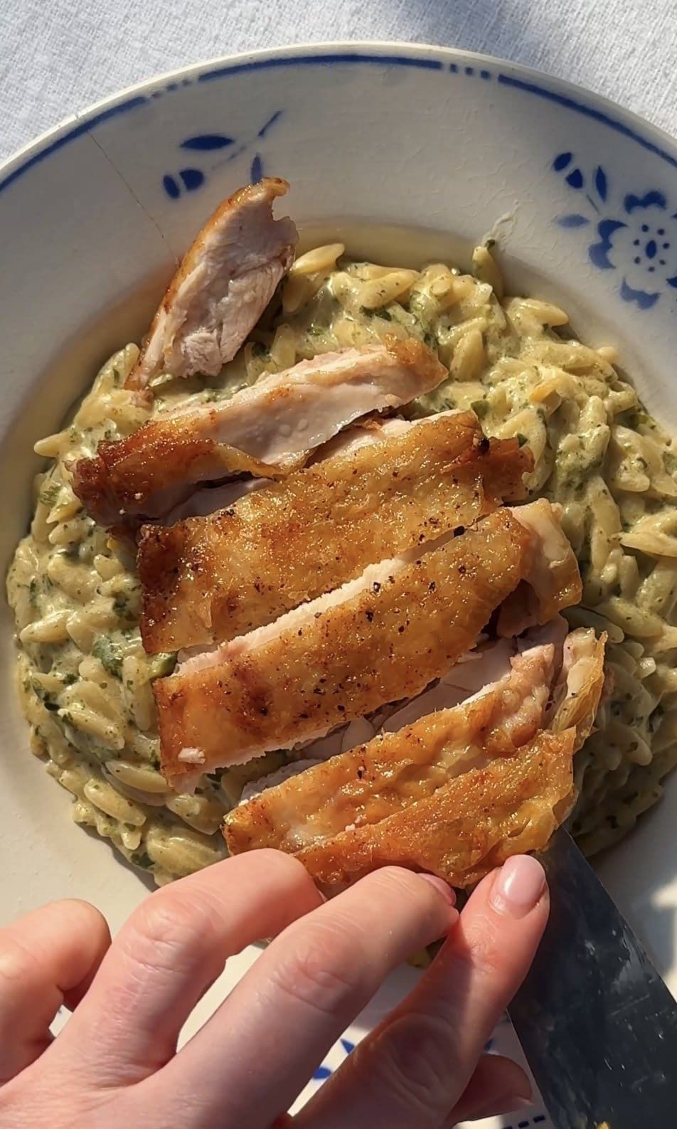 Topping lemon-infused orzo with sliced chicken thighs on plate.