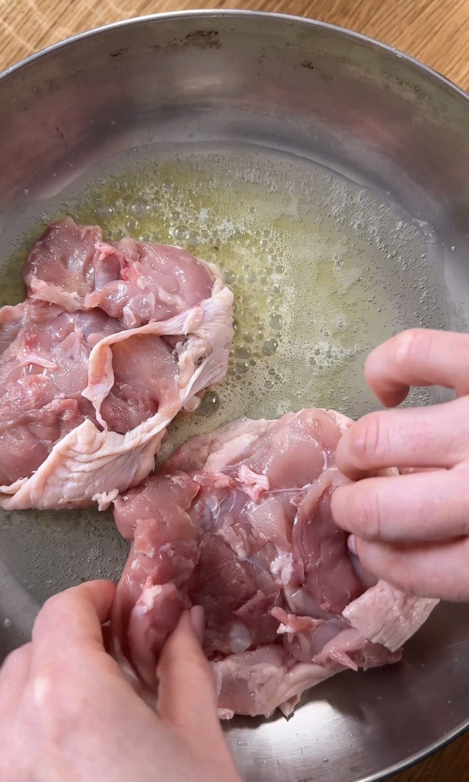 Chicken thighs searing skin-side down in a pan.