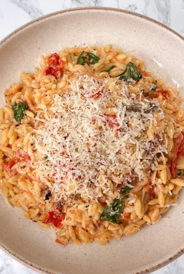 Bowl of tomato orzo with basil topped with grated parmesan.