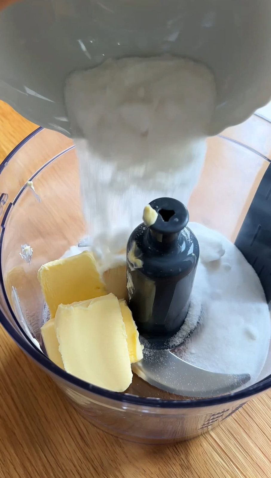 Adding sugar to the food processor with butter.