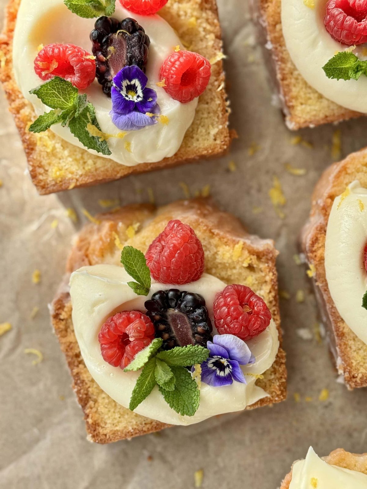 Slices of lemon loaf cake topped with icing, fruit, and flowers.