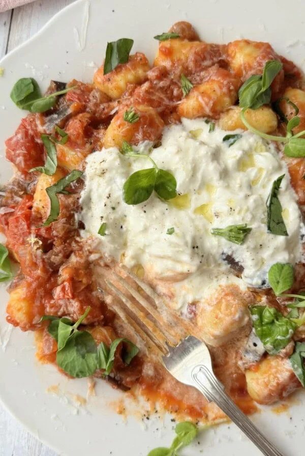 gnocchi alla norma on a white plate with burrata and fresh basil on top