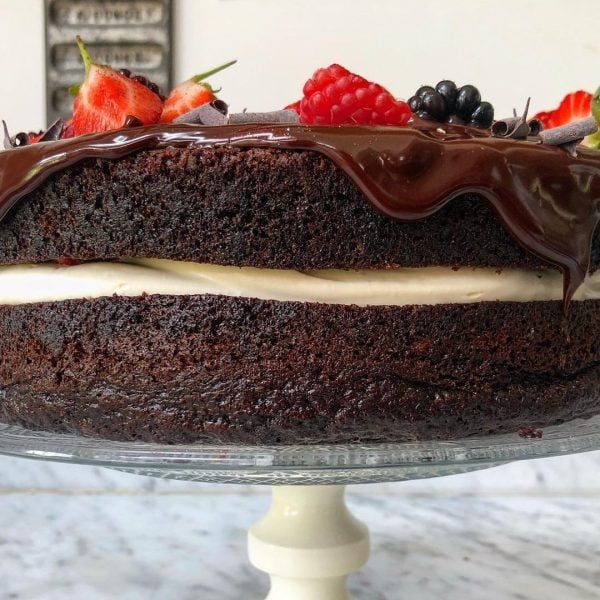 Side angle of moist chocolate cake filled with cream and topped with berries and ganache