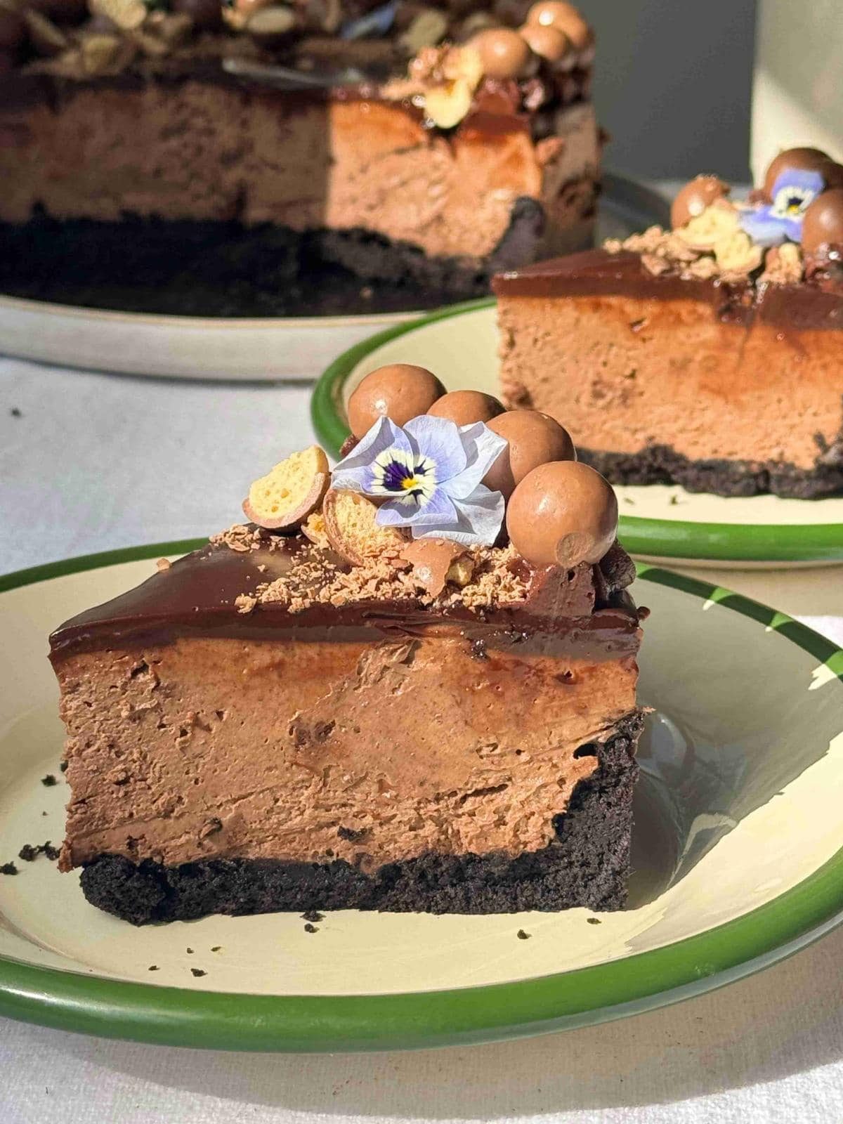 slice of no-bake chocolate cheesecake on a white plate with green rim.