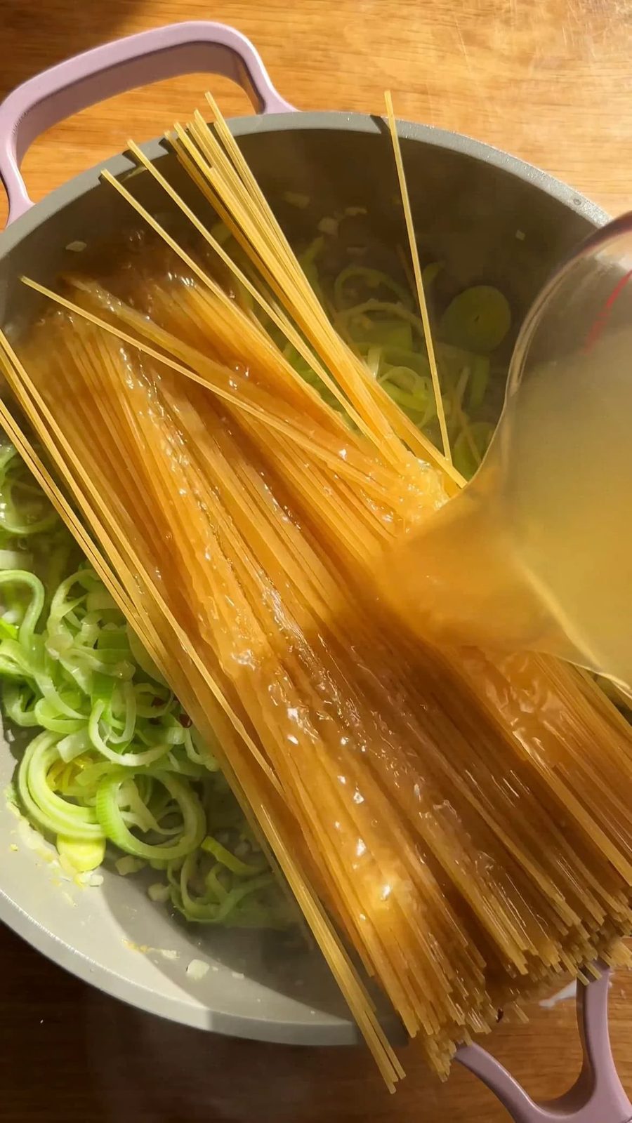adding stock to pasta in a large saucepan