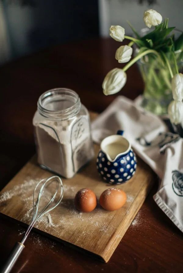 A jar of flour and a jug of milk on a wooden board.