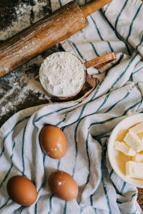 a photo of eggs, a cup of flour and softened butter on a tea towel