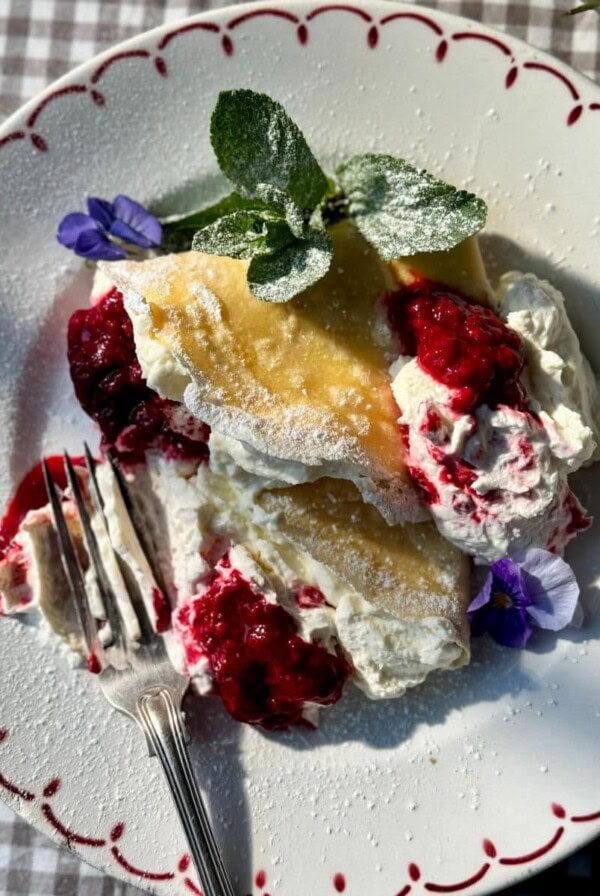 berry crepes on plate with raspberries and whipped cream.