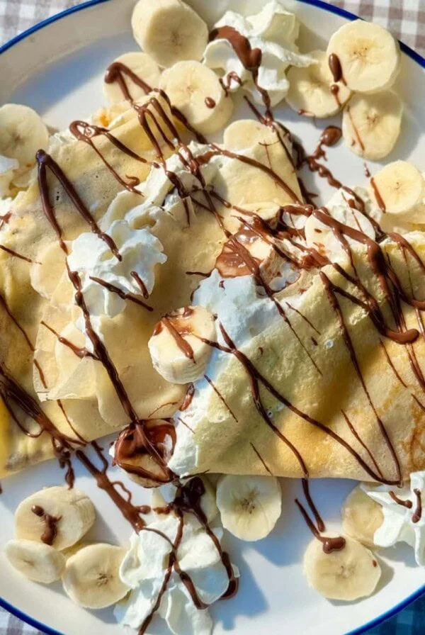 banana crepes on white plate with whipped cream and nutella.