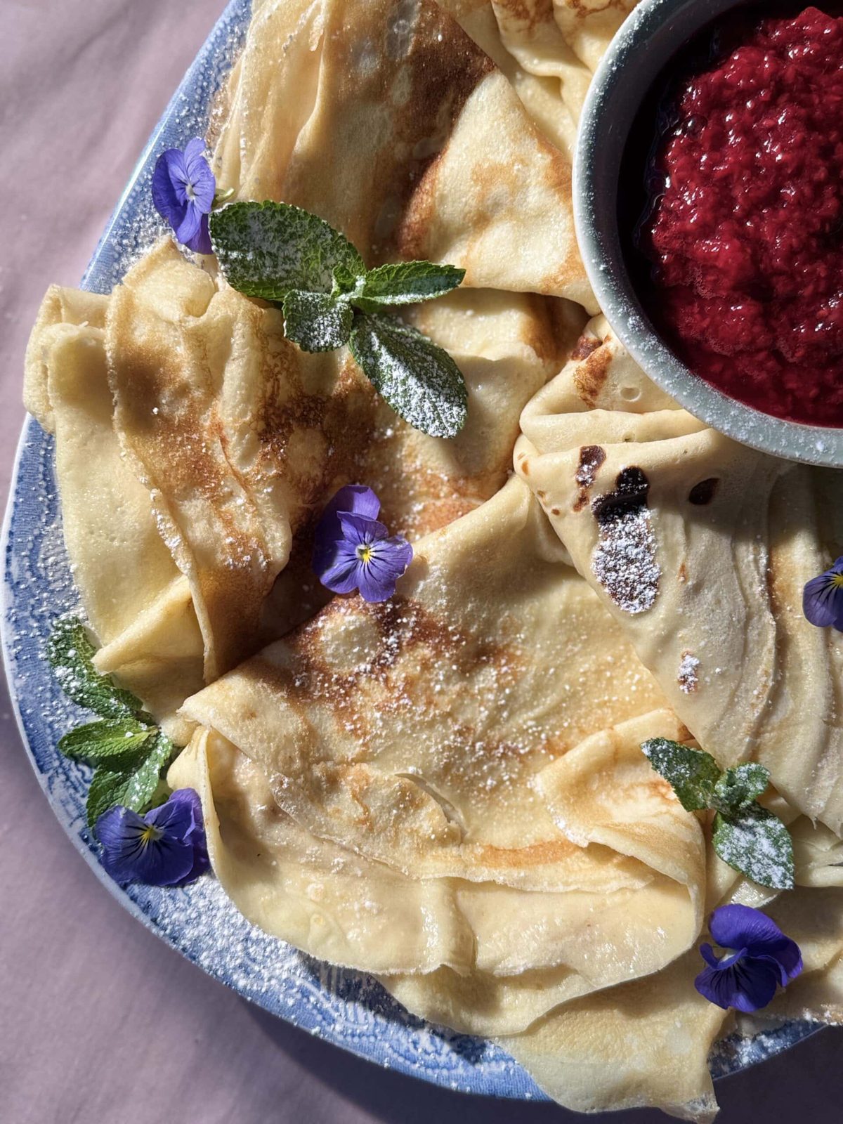 pannekaker on blue plate with raspberry compote.