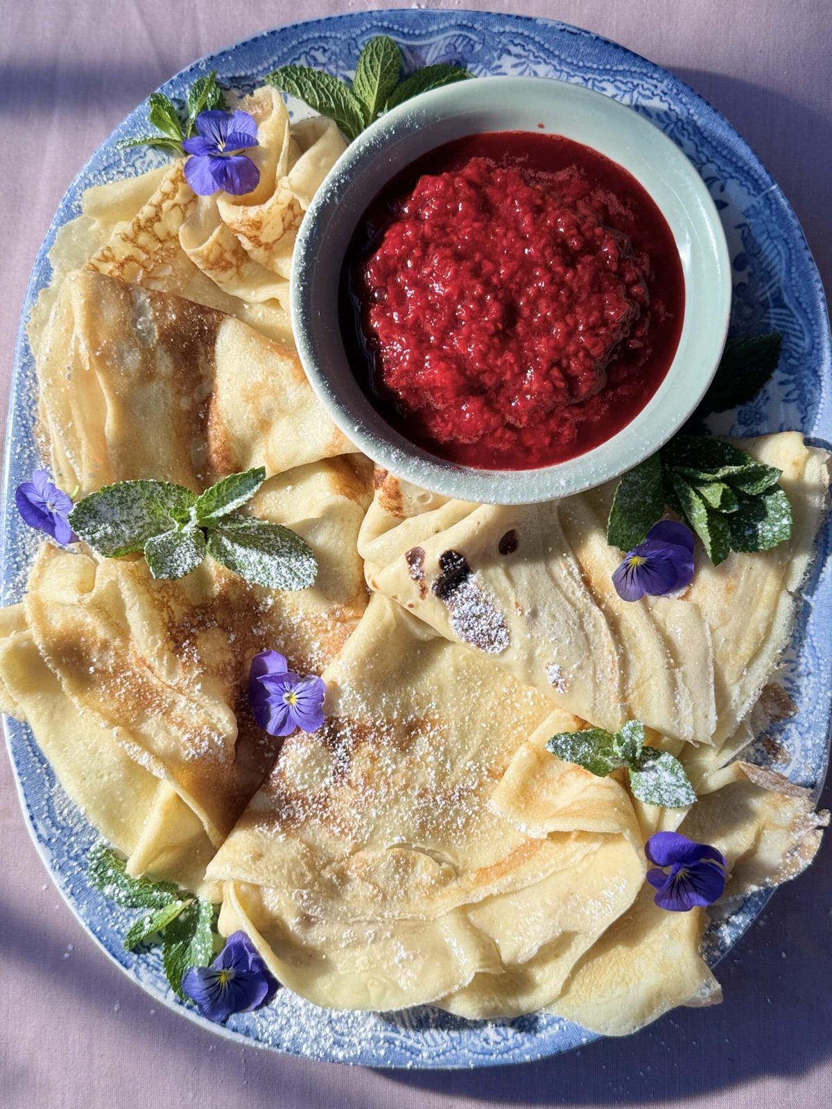 pannekaker on blue plate with raspberry compote.
