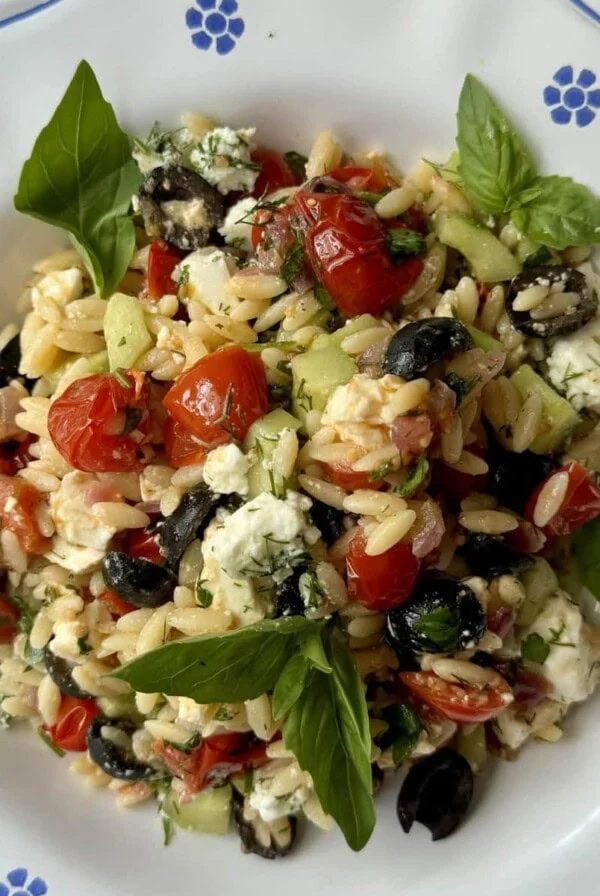 greek pasta salad in white bowl with blue flowers.