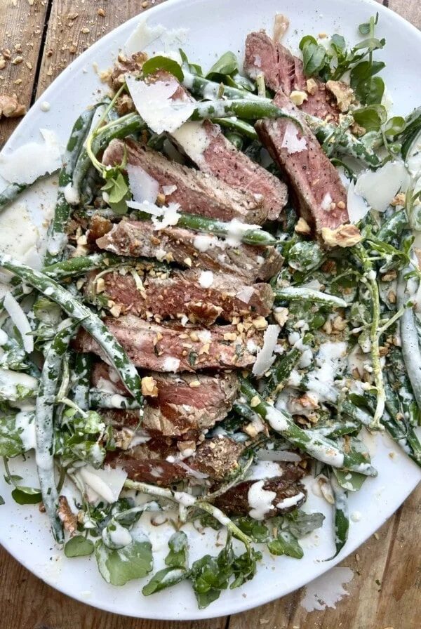 White serving platter with a steak and green bean caesar salad.