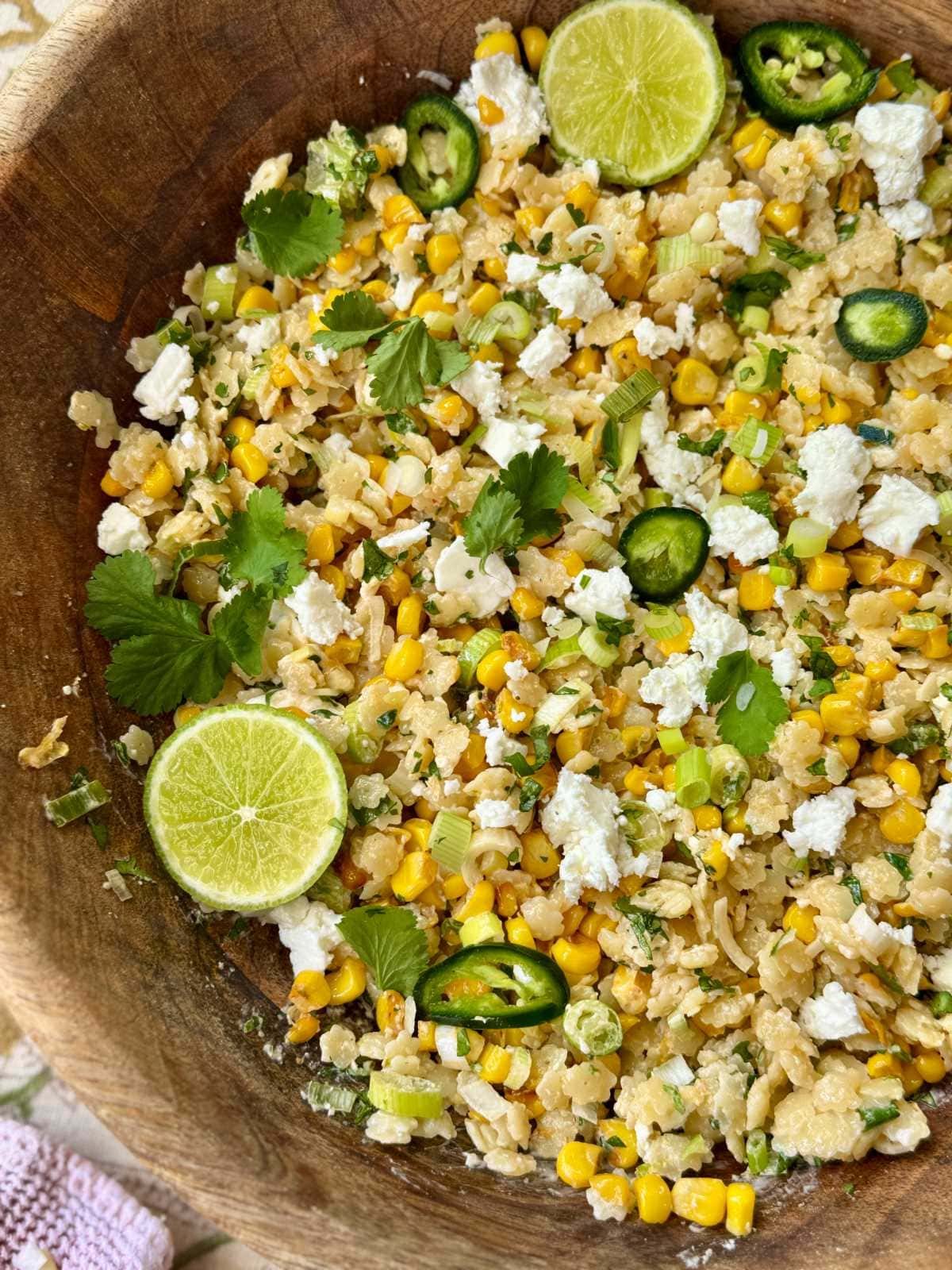 pastina salad in a wooden bowl with lime slices and feta.