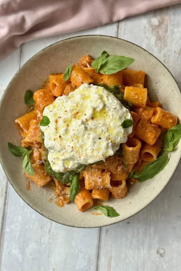 chicken and vodka pasta scooped into bowl with pesto and burrata on top.