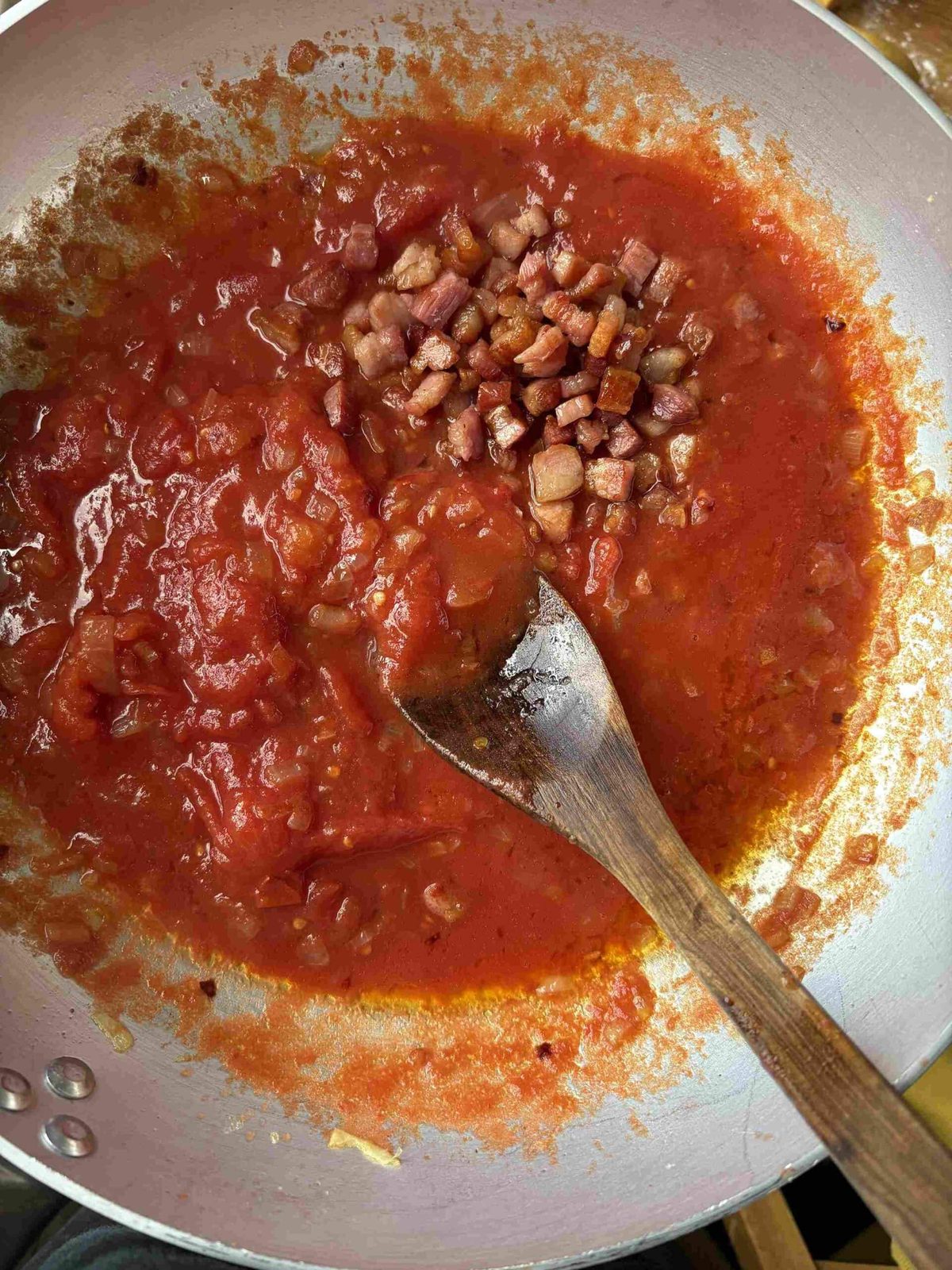 Stirring guanciale into tomato pasta sauce.