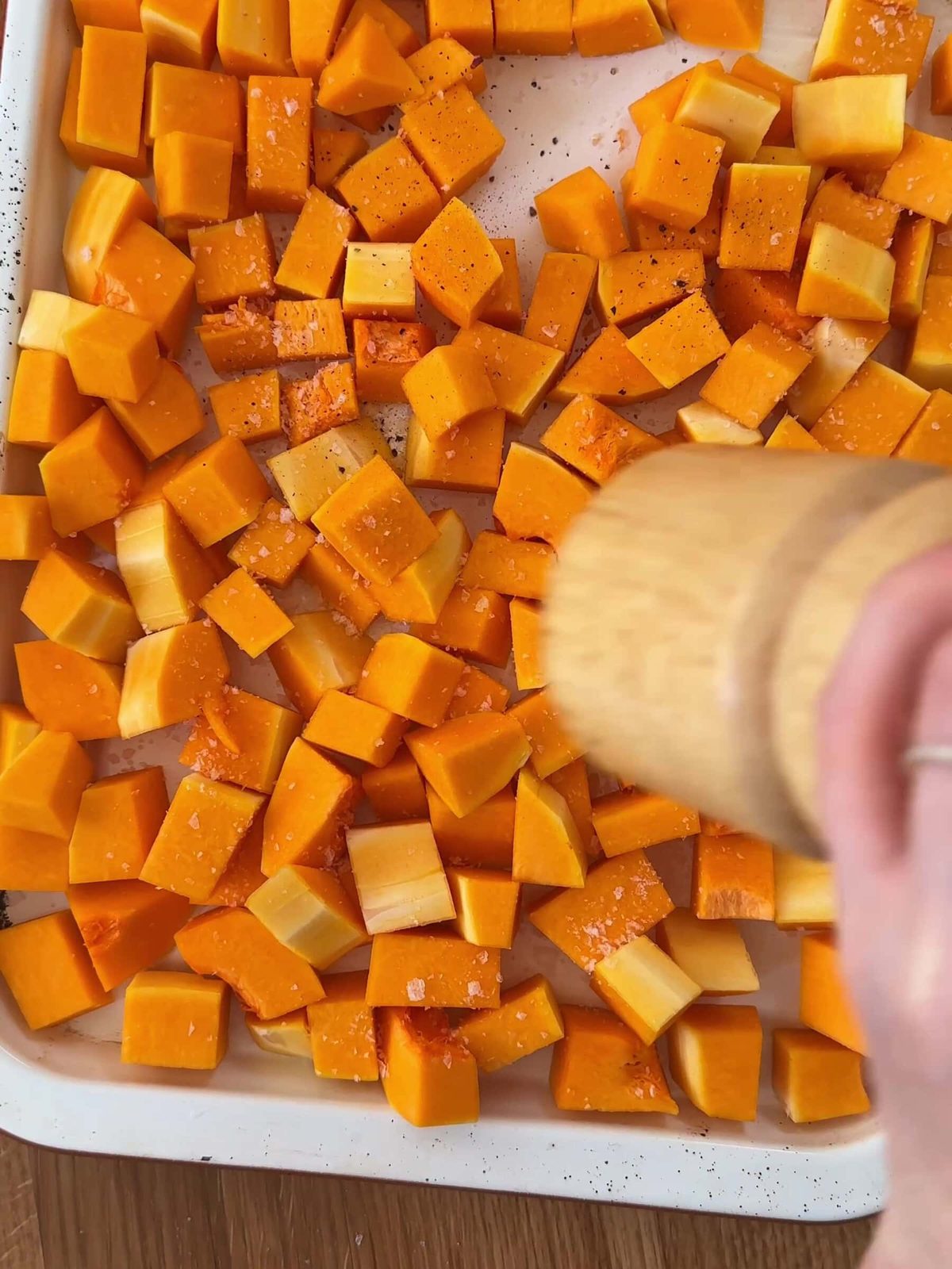 Seasoning cubed butternut squash on baking sheet.