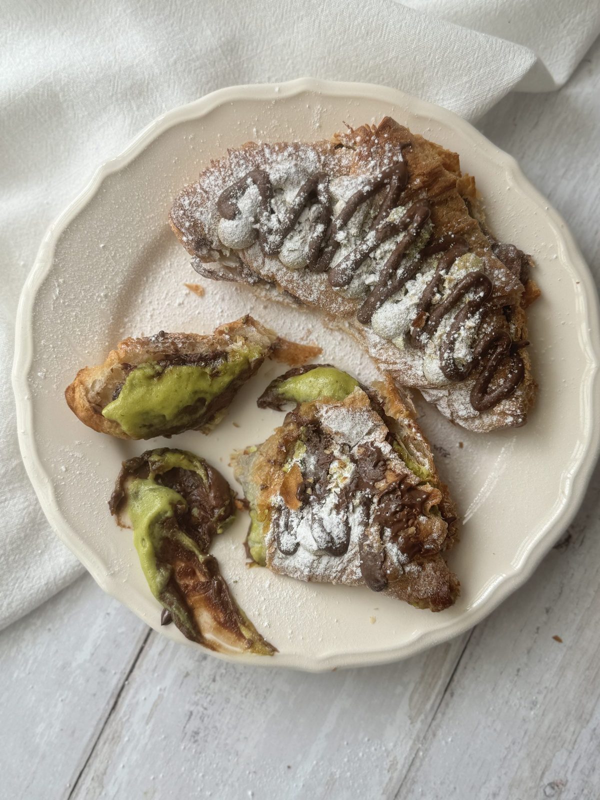 Two pistachio croissants on a white plate.