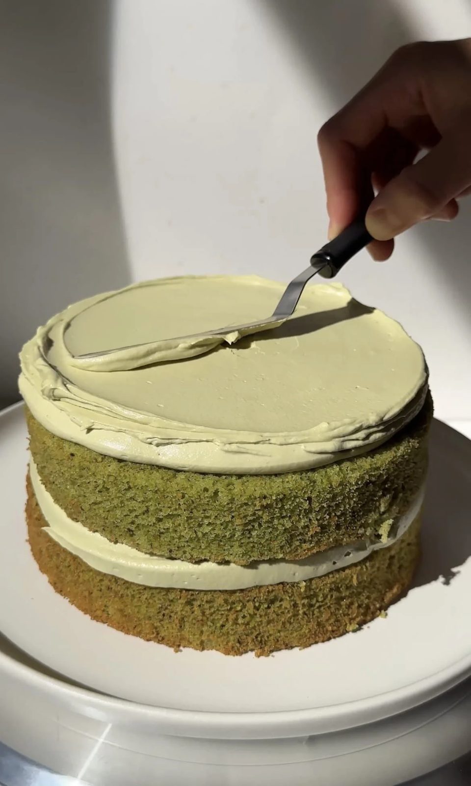 Smoothing pistachio icing onto the tiered cake.