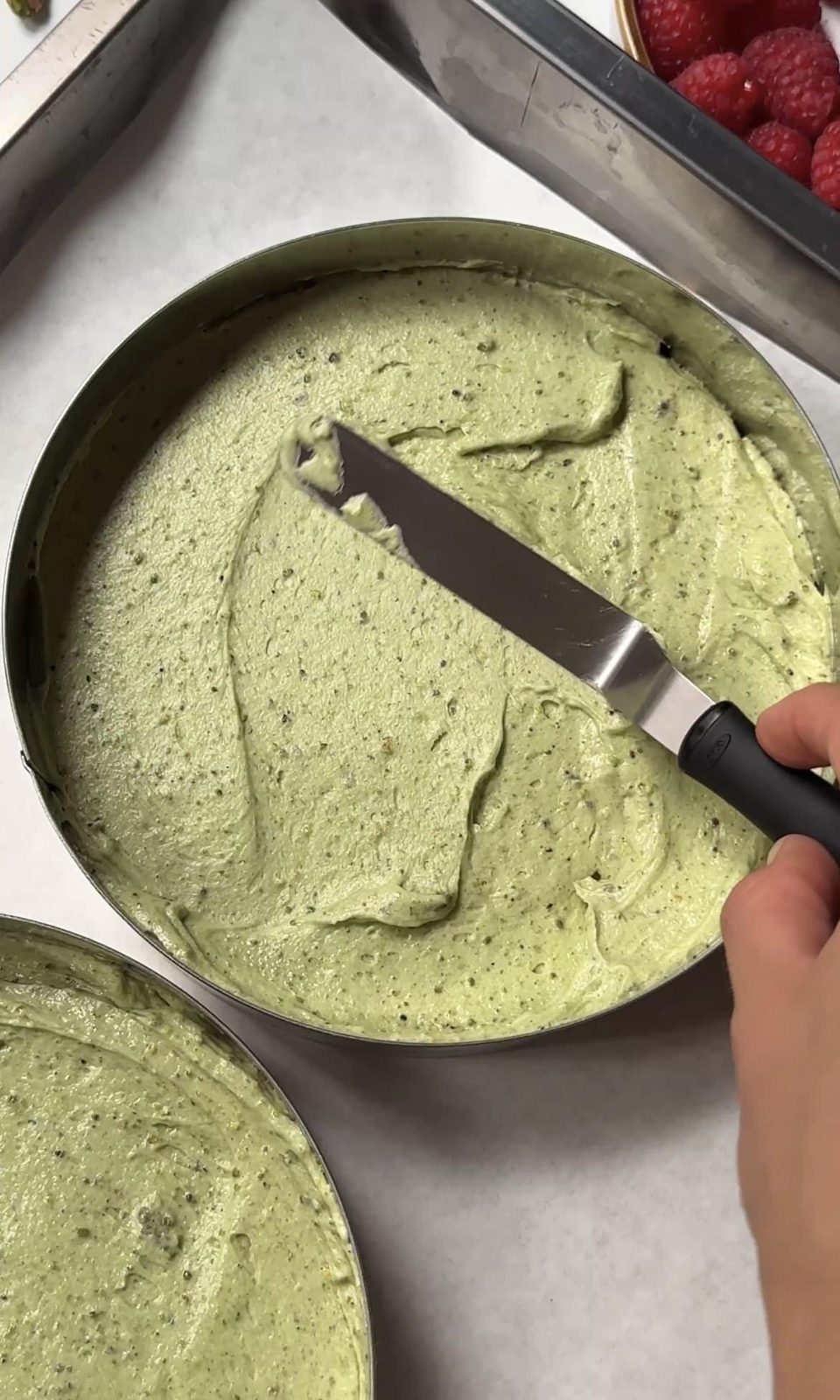Smoothing pistachio cake batter into round cake pans.