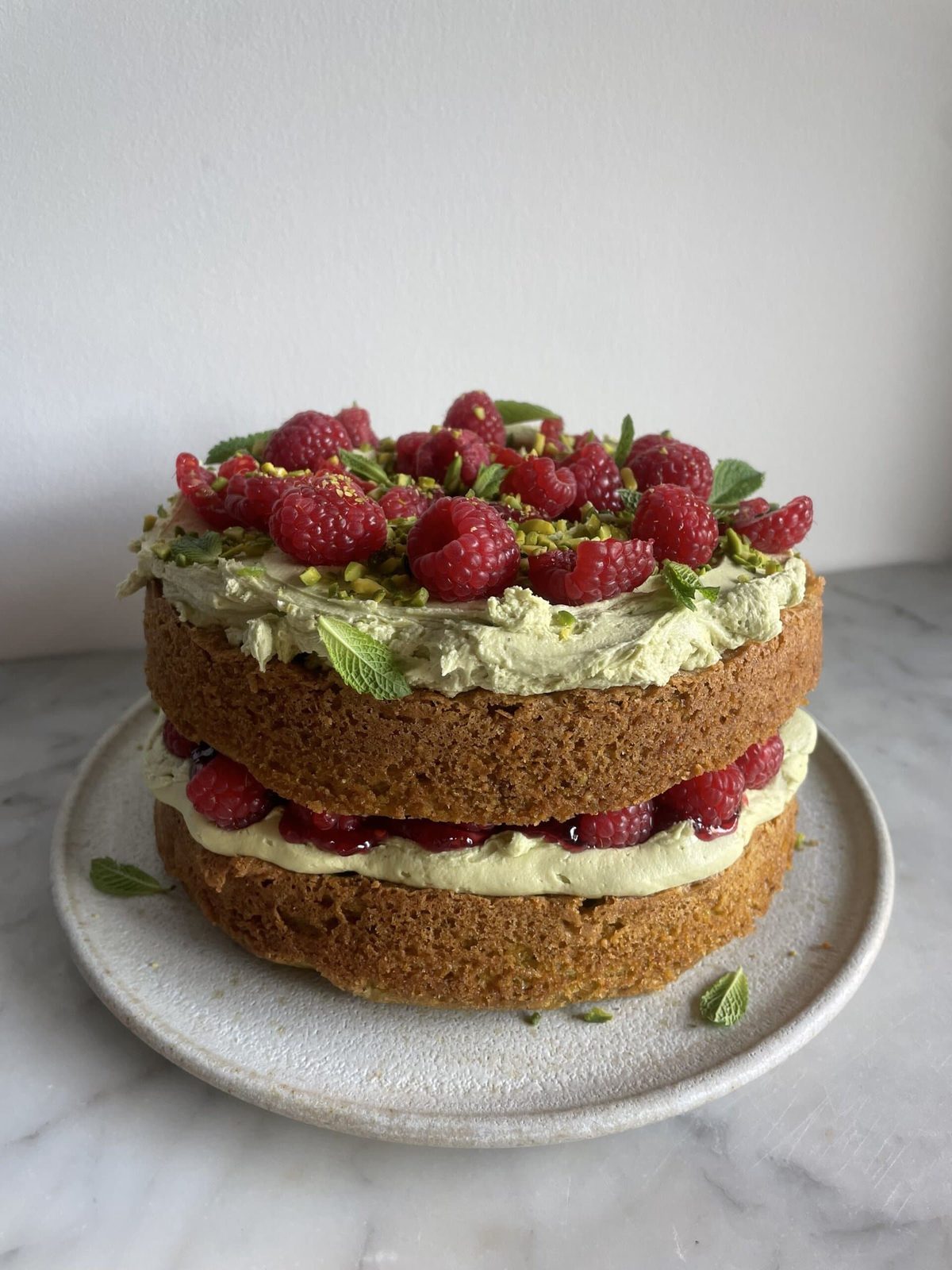 Layered cake with pistachio cream and raspberries on plate.