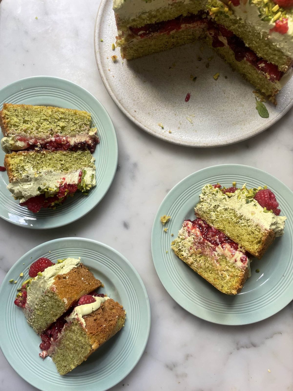 Slices of pistachio raspberry cake on blue plates.
