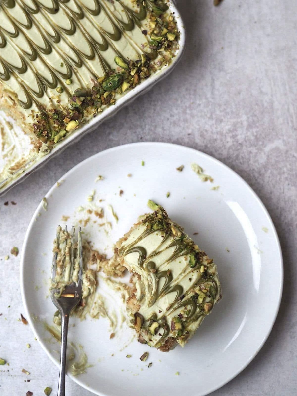 Pistachio tiramisu in white dish with slice on a plate.