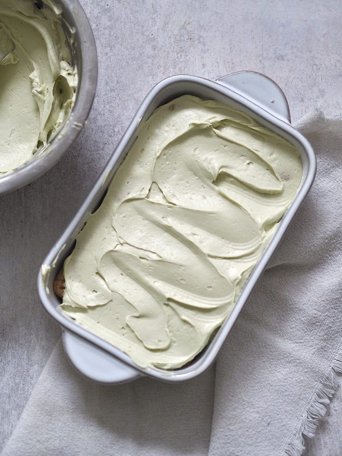 Layered pistachio tiramisu in pan with pistachio cream top.