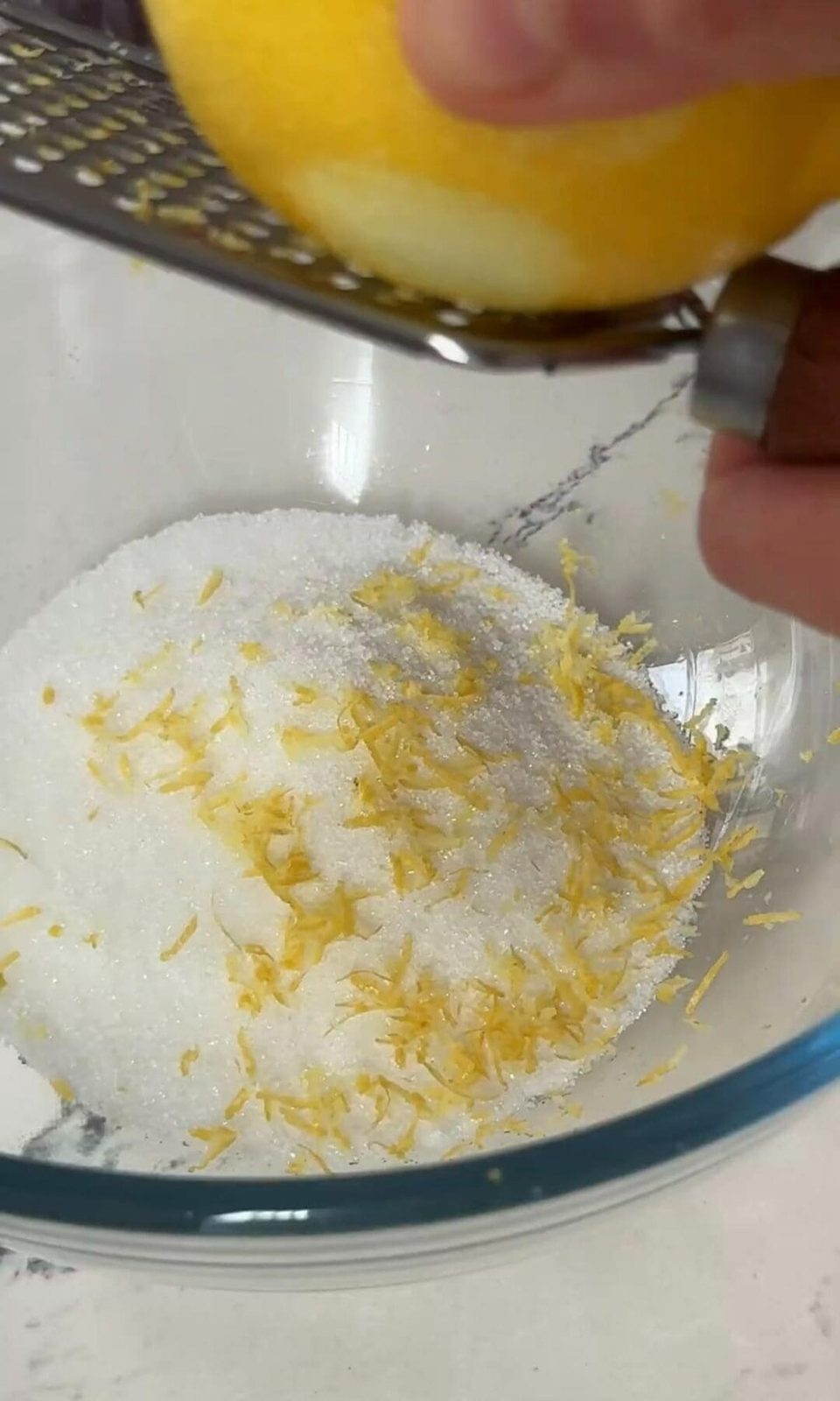 Grating lemon zest over bowl of sugar.