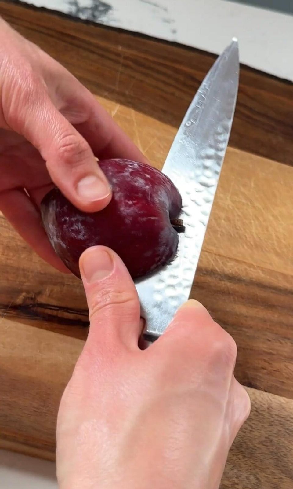 Slicing plum in half with large knife.