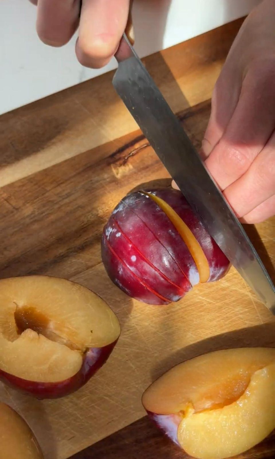 Slicing fresh plums on cutting board with chef's knife.
