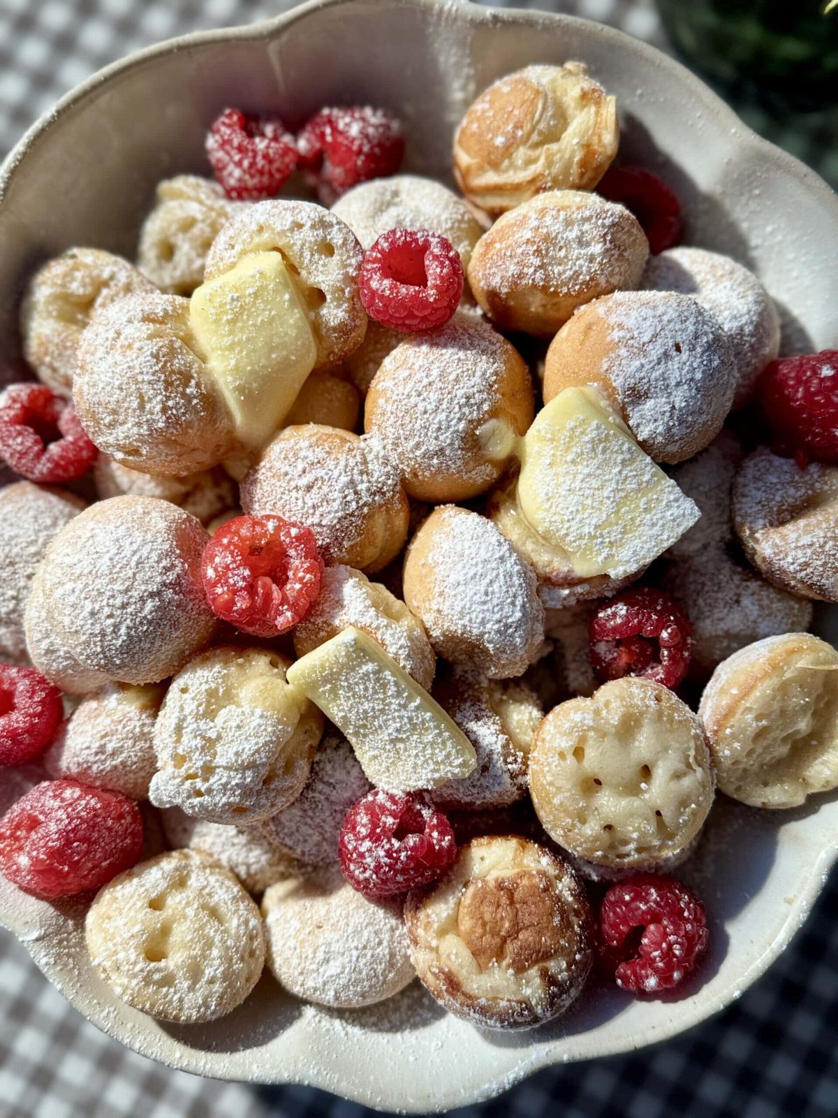 Poffertjes in bowl with butter and raspberries.