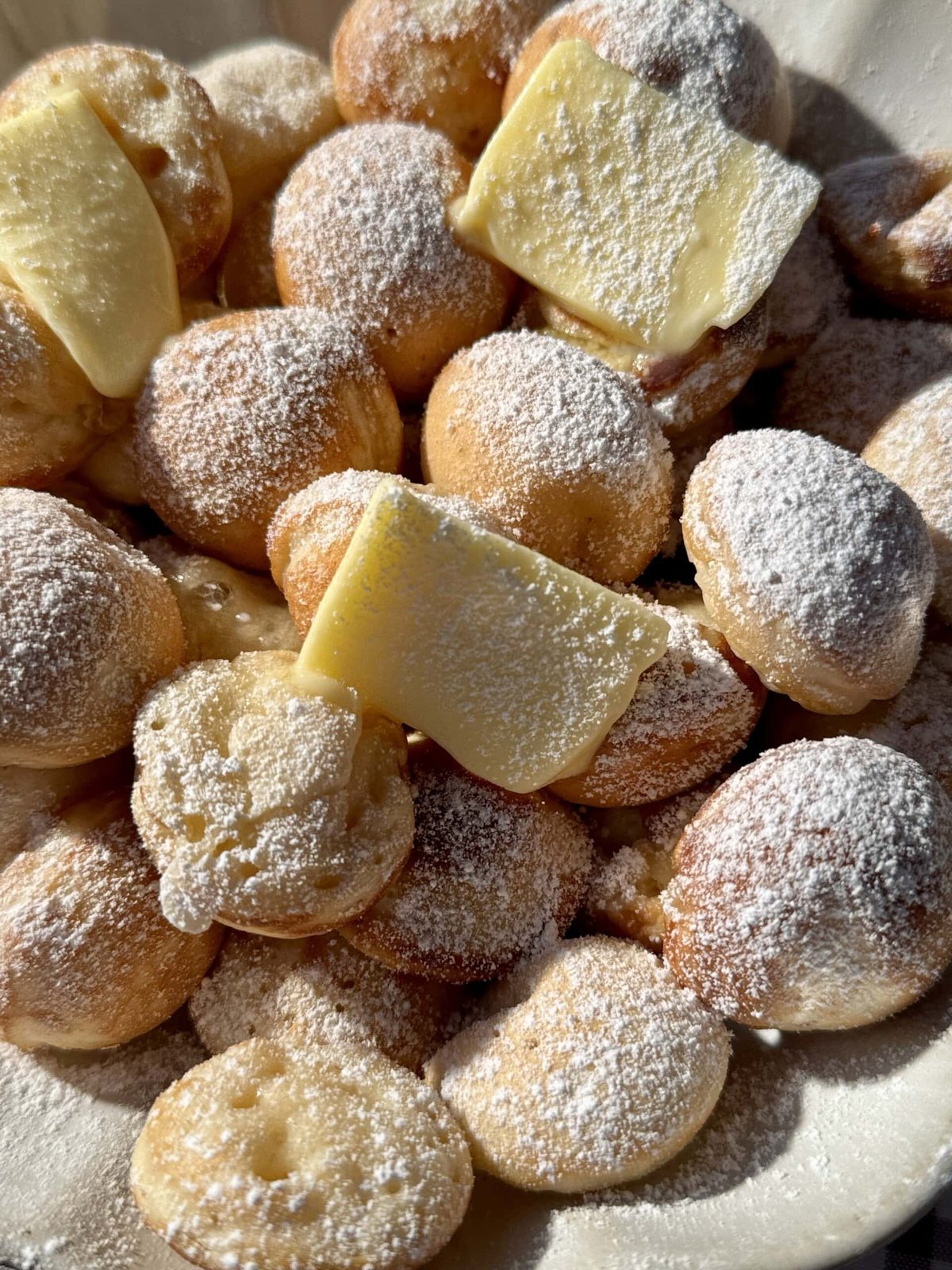 Poffertjes in bowl with butter and icing sugar.