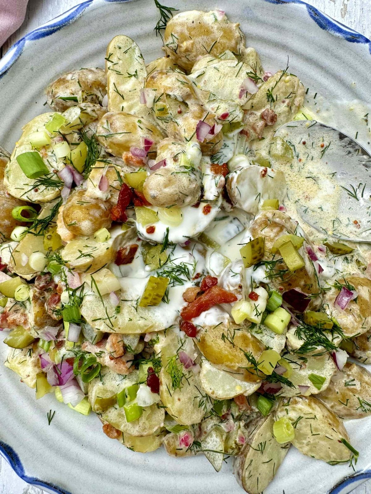 potato salad with dill and pickles in a bowl with spoon.