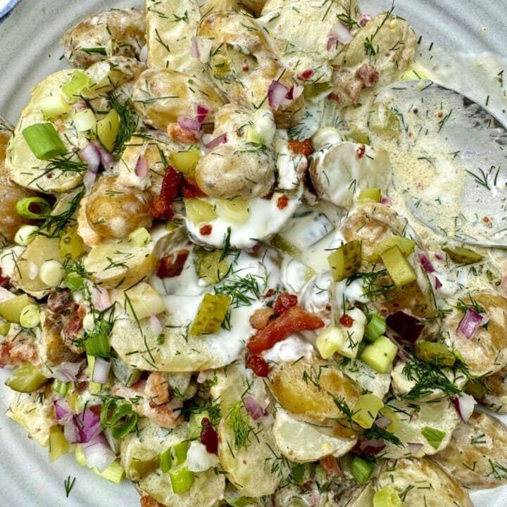 potato salad with dill and pickles in a bowl with spoon.