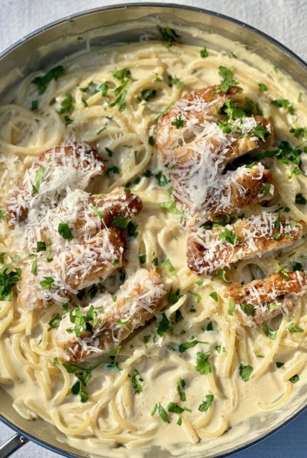 Creamy chicken pasta in a pan with a fork, with chicken sliced on top..