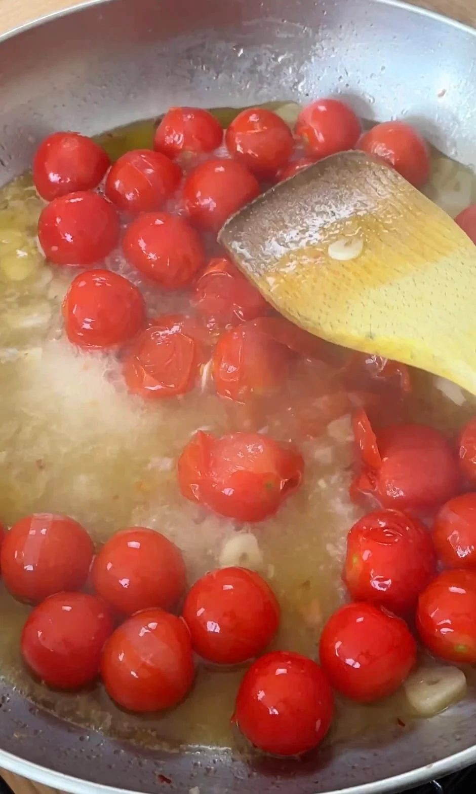 Smashing cherry tomatoes in sauce with a spoon.