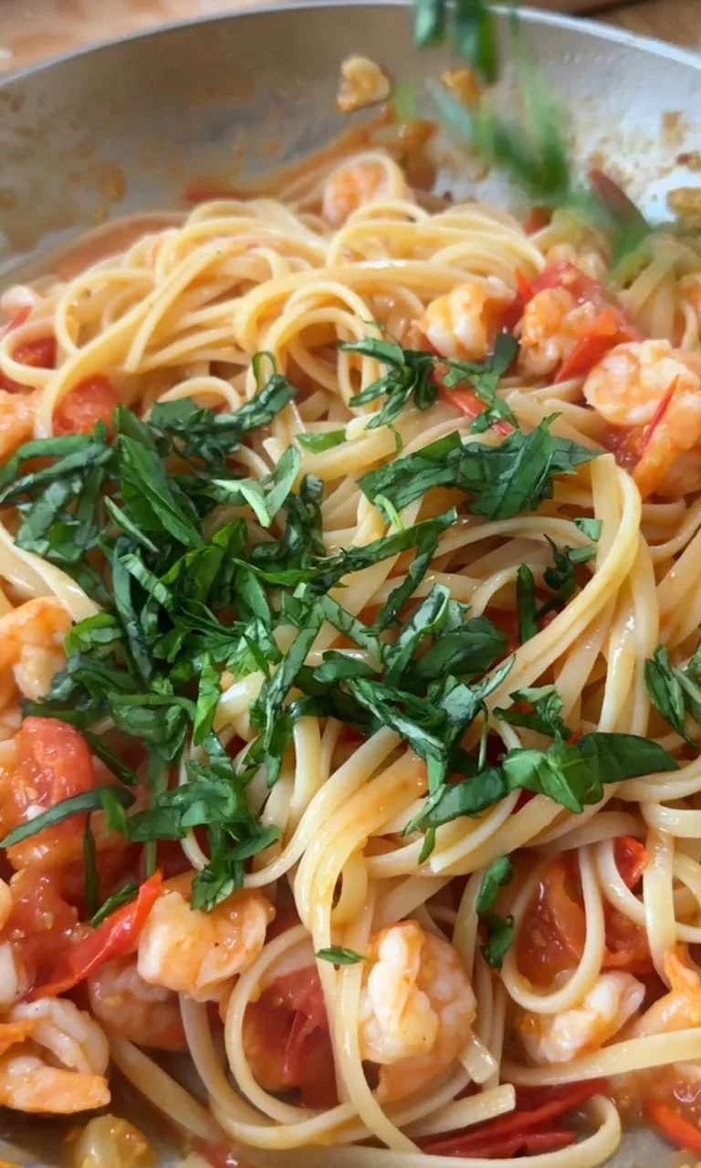 Adding fresh basil to shrimp, tomato, and linguine.