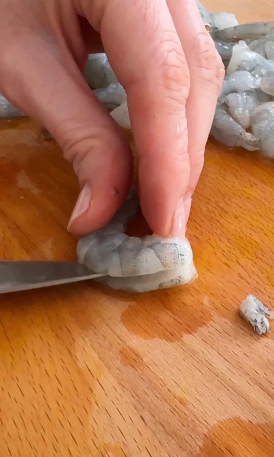 Butterflying prawns with knife on cutting board.
