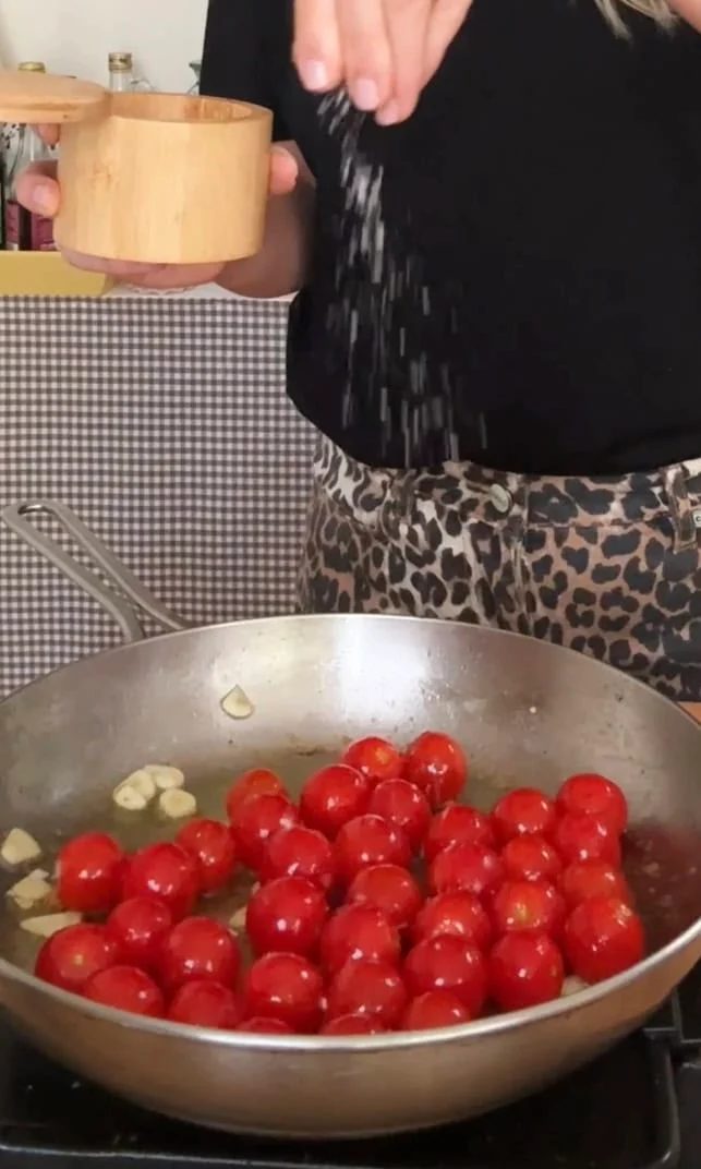 Seasoning cherry tomatoes with salt in large pan.