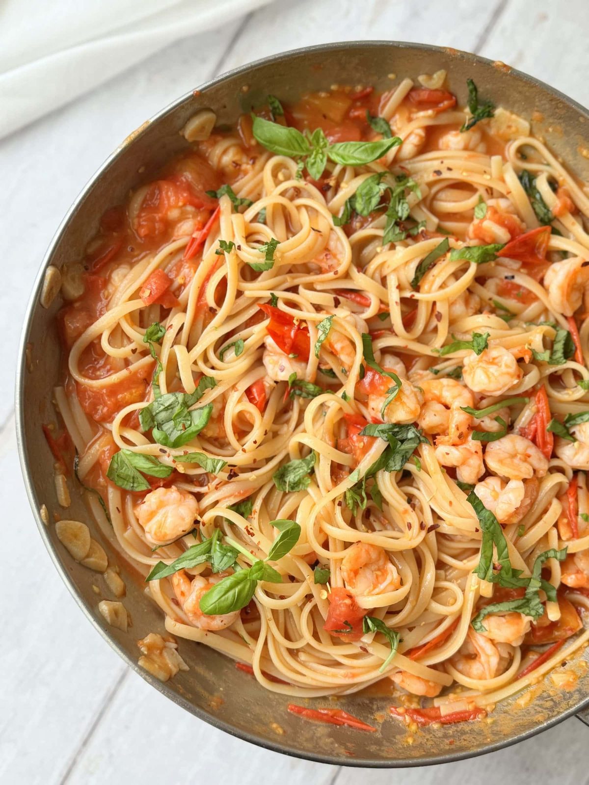 Pan of prawn tomato linguine on a white table with fresh basil leaves.