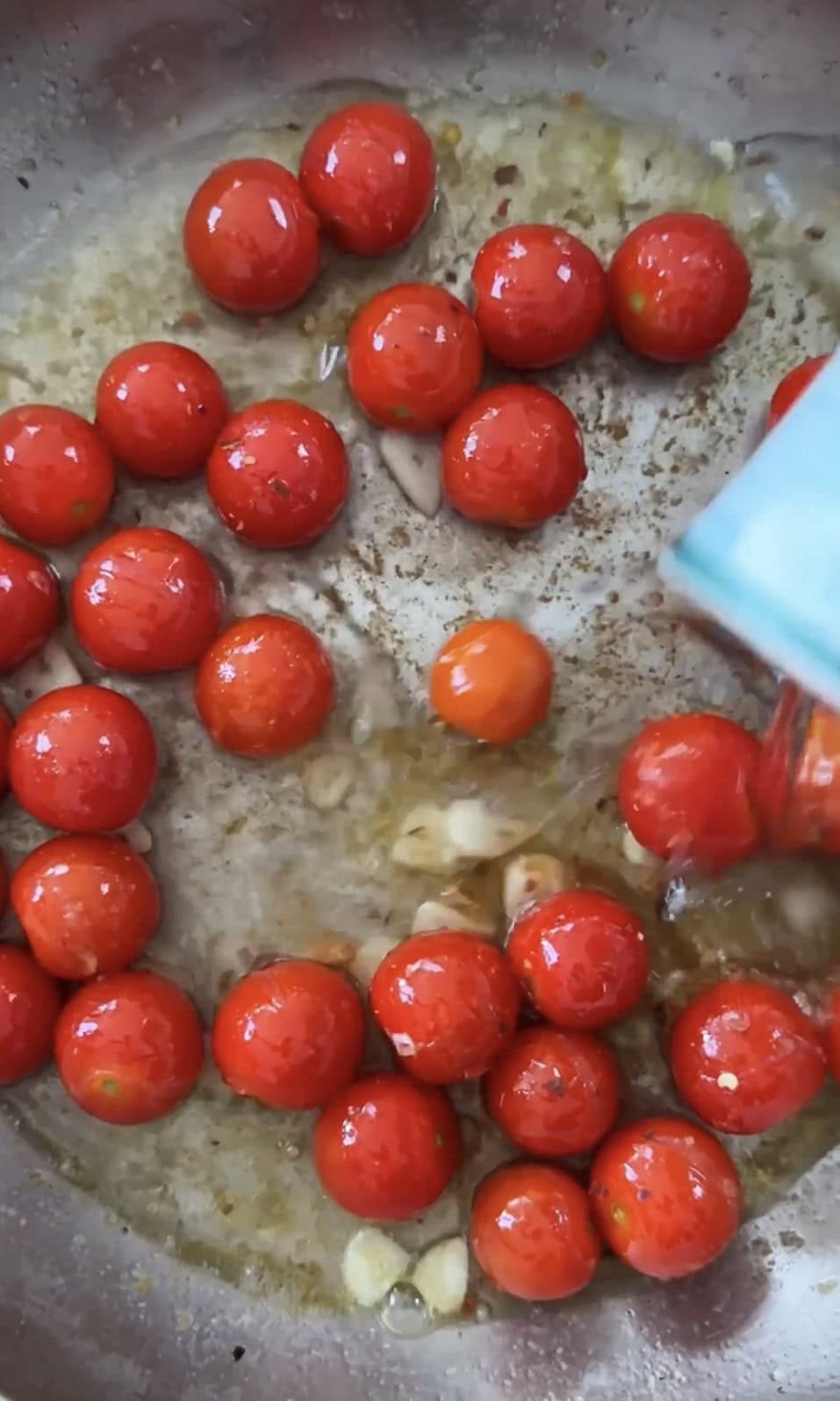 Adding pasta water to cherry tomatoes and garlic in pan.