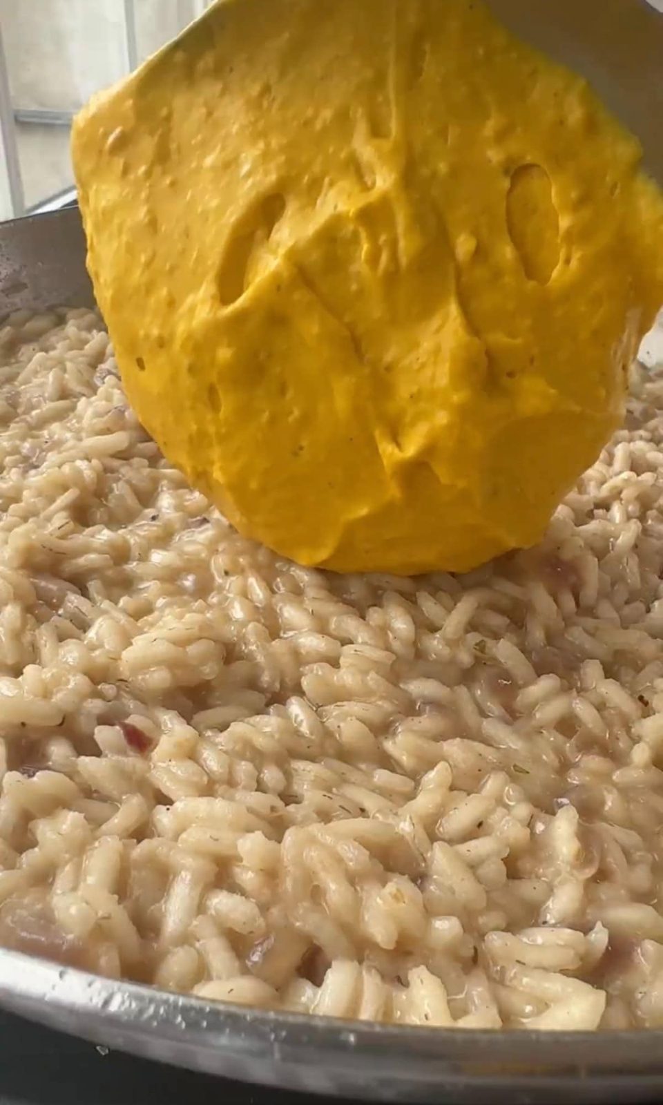 Adding pumpkin puree into pan with cooking risotto.