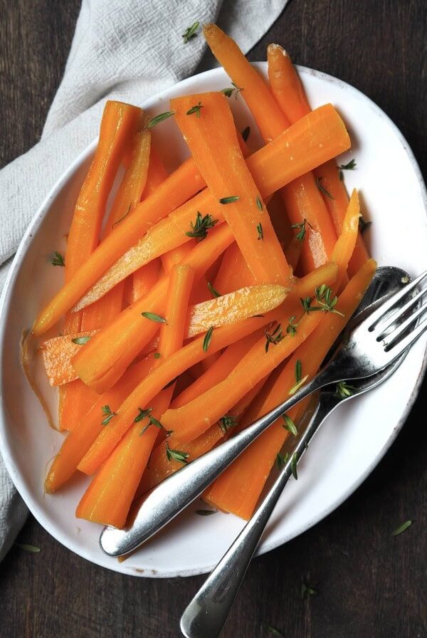 White serving dish of glazed carrots with fresh thyme sprinkled over the top.