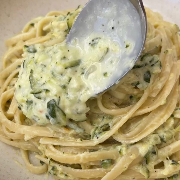 spooning sauce over courgette pasta in a beige bowl.