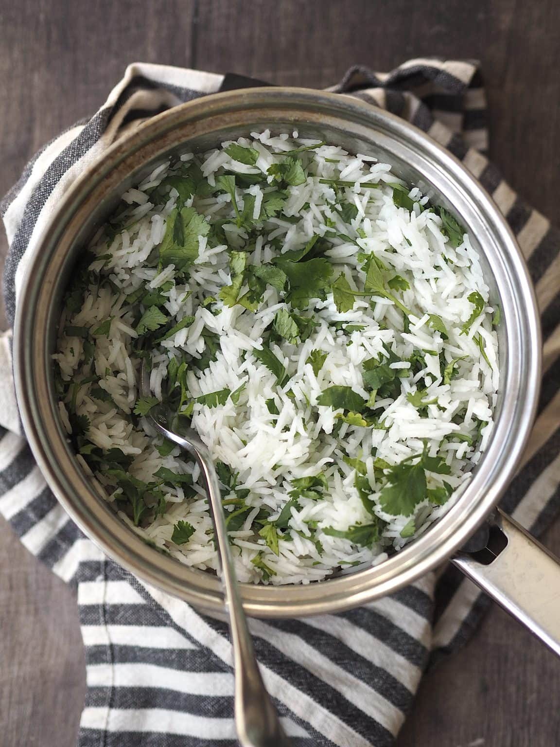 Saucepan of herby rice on top of a blue and white striped tea towel.
