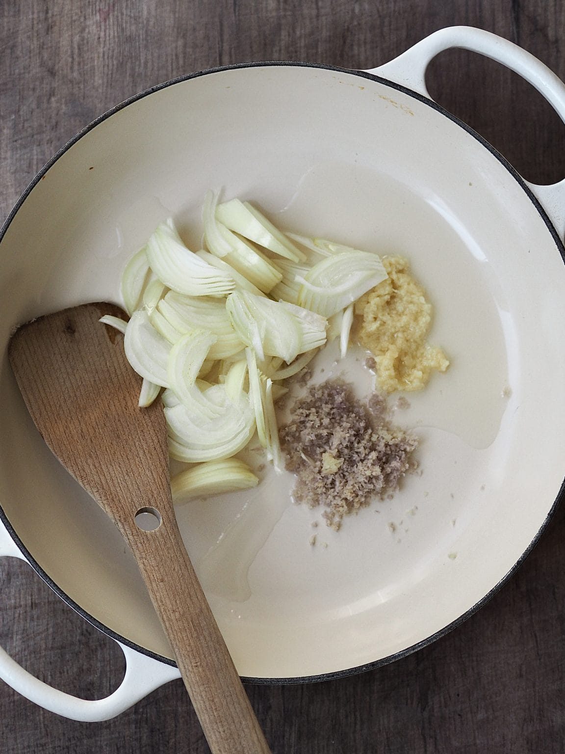 Sliced onions, ginger, garlic and spices in a shallow casserole dish.