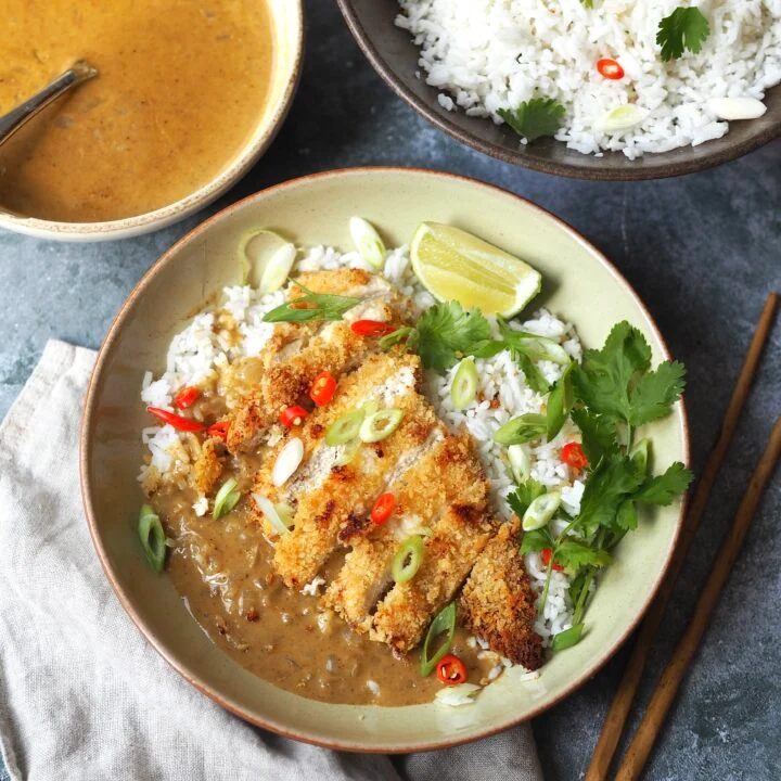 A chicken katsu curry bowl next to serving bowls of herbed rice and Japanese coconut curry sauce.
